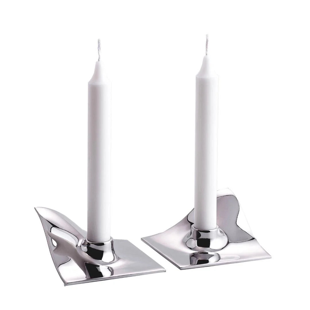 Two white taper candles in polished silver metal holders with an abstract, wavy base design, shown on a plain white background.