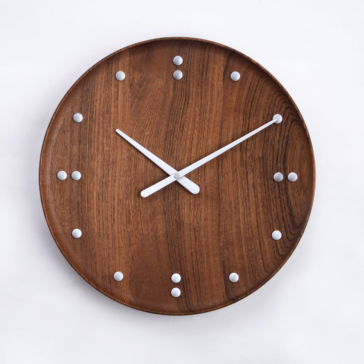 A round wooden wall clock with a teak wood grain finish, minimalist silver hands, and small silver dot hour markers, shown against a plain white background.