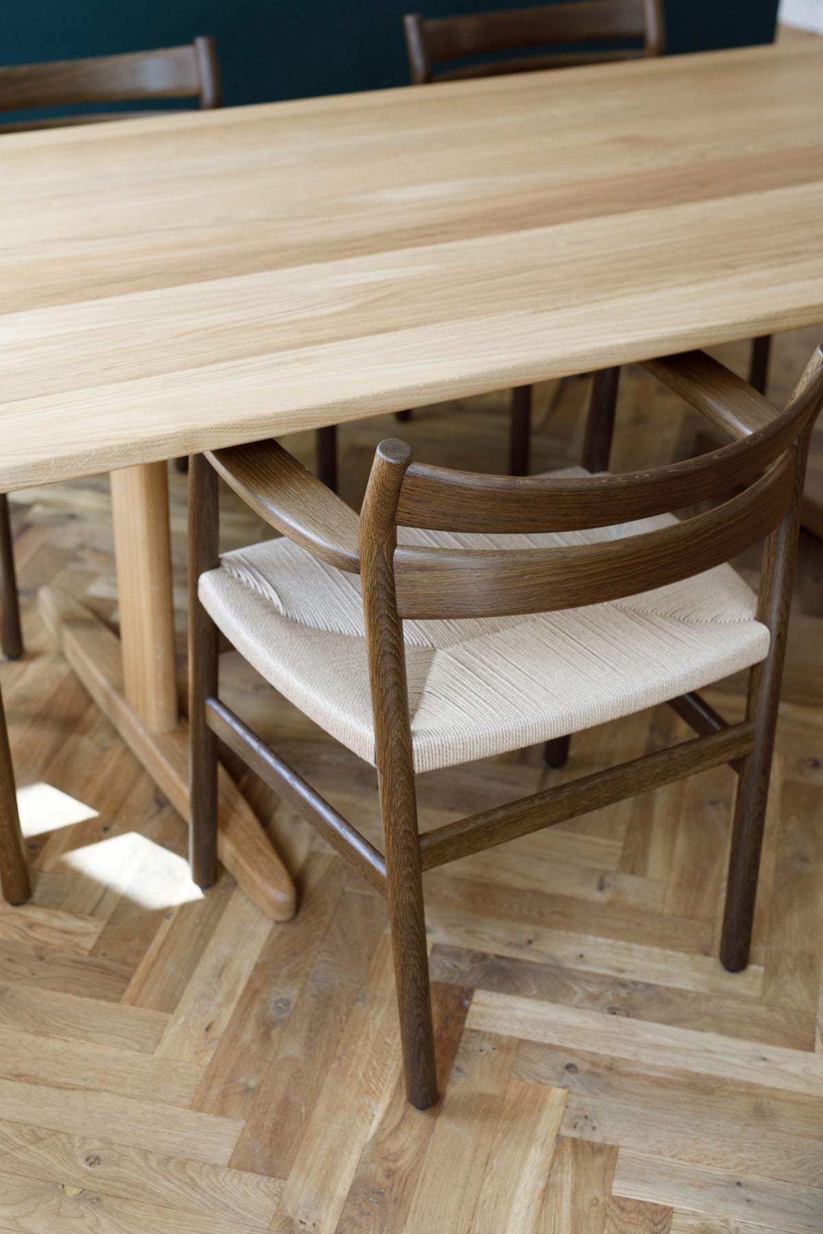 A close-up of a wooden dining table and chairs in a dining room setting with a herringbone wood floor.