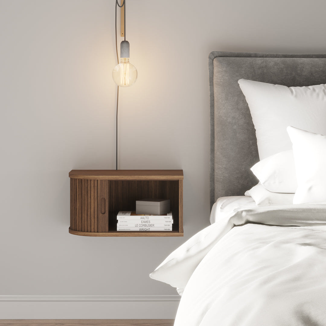 Bedroom with wooden nightstand and wall lamp next to a bed with white bedding.