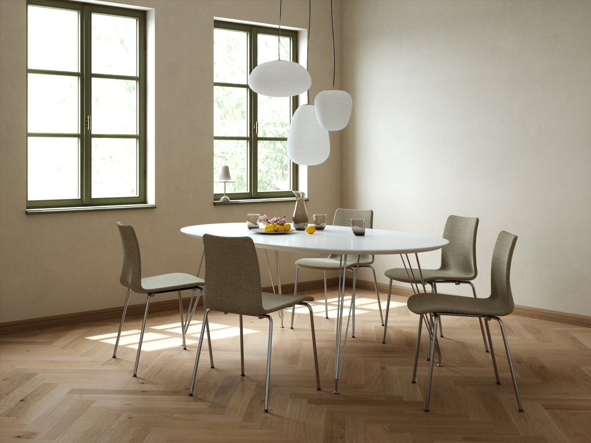 A modern dining room scene featuring a round white table surrounded by six contemporary chairs with textured taupe-gray upholstery and slim metal legs. The room has light beige walls, a herringbone wood floor, and two tall windows with green frames, illuminated by three white spherical pendant lights.