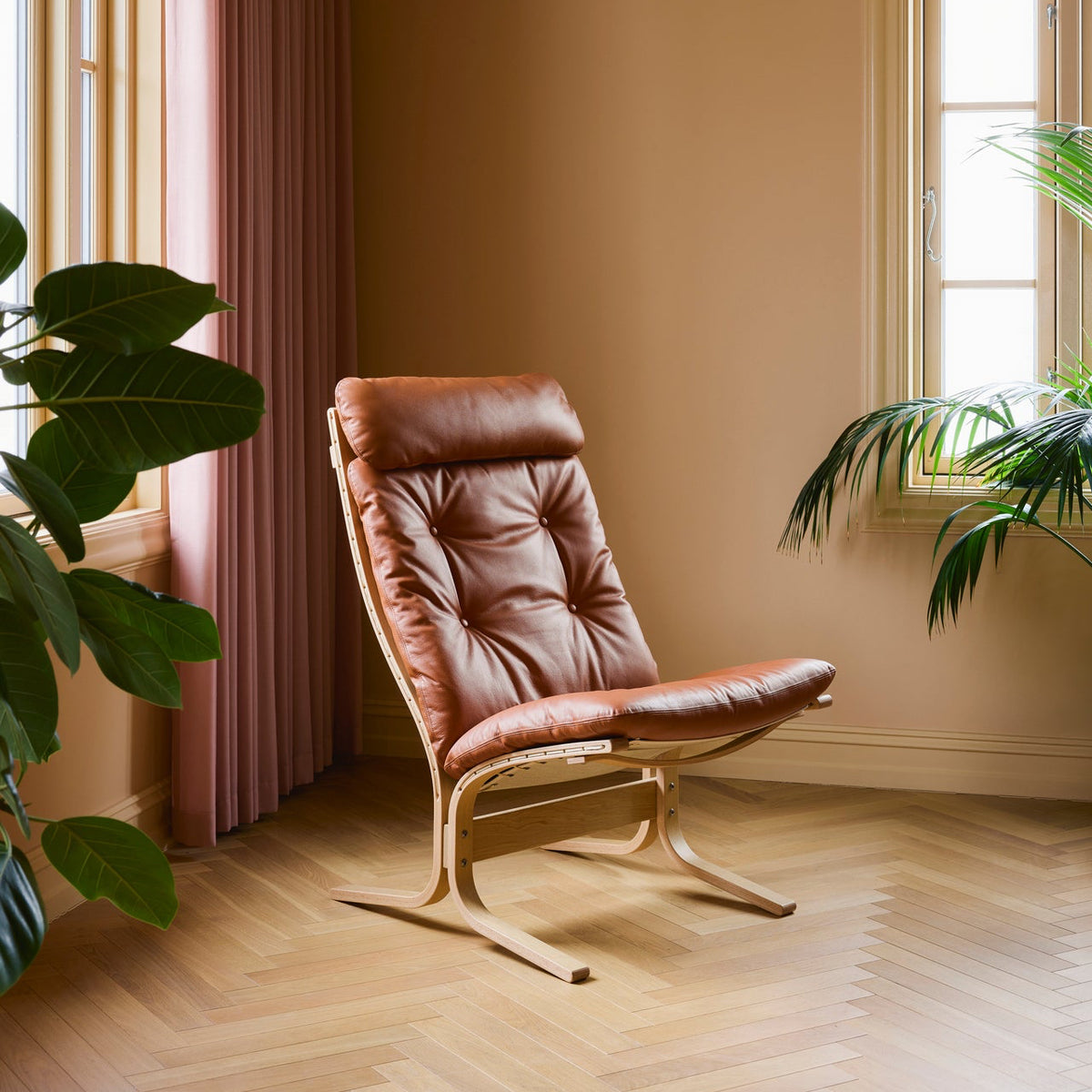 Brown leather chair in a room with beige walls, pink curtains, and plants.