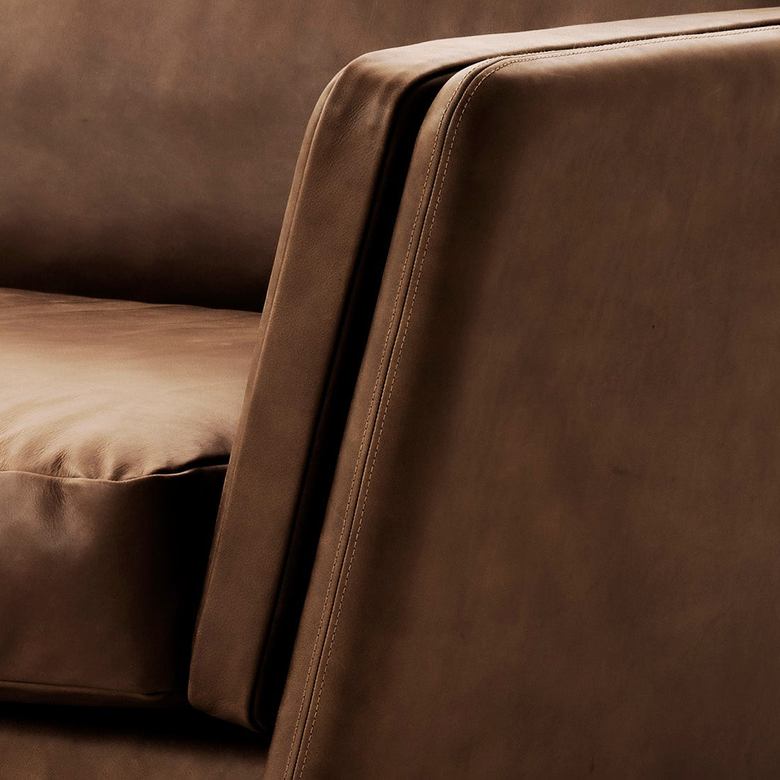 Close-up of a brown upholstered sofa showing the seat cushion, back cushion, and armrest with a smooth leather-like texture.