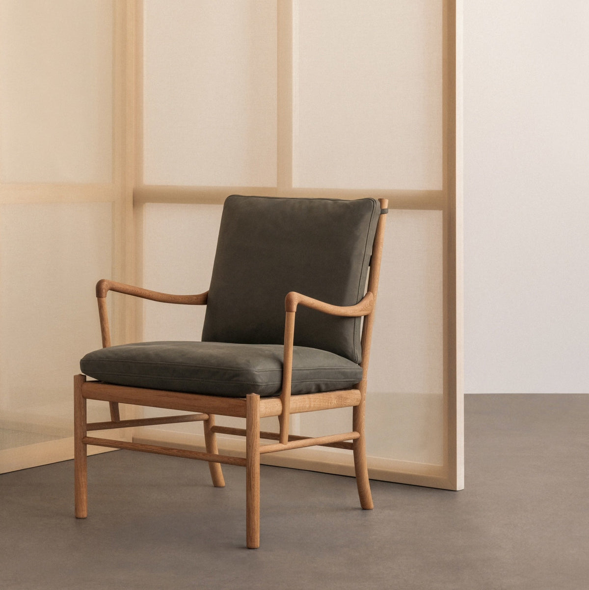 Chair with wooden frame and dark cushions against a neutral wall.