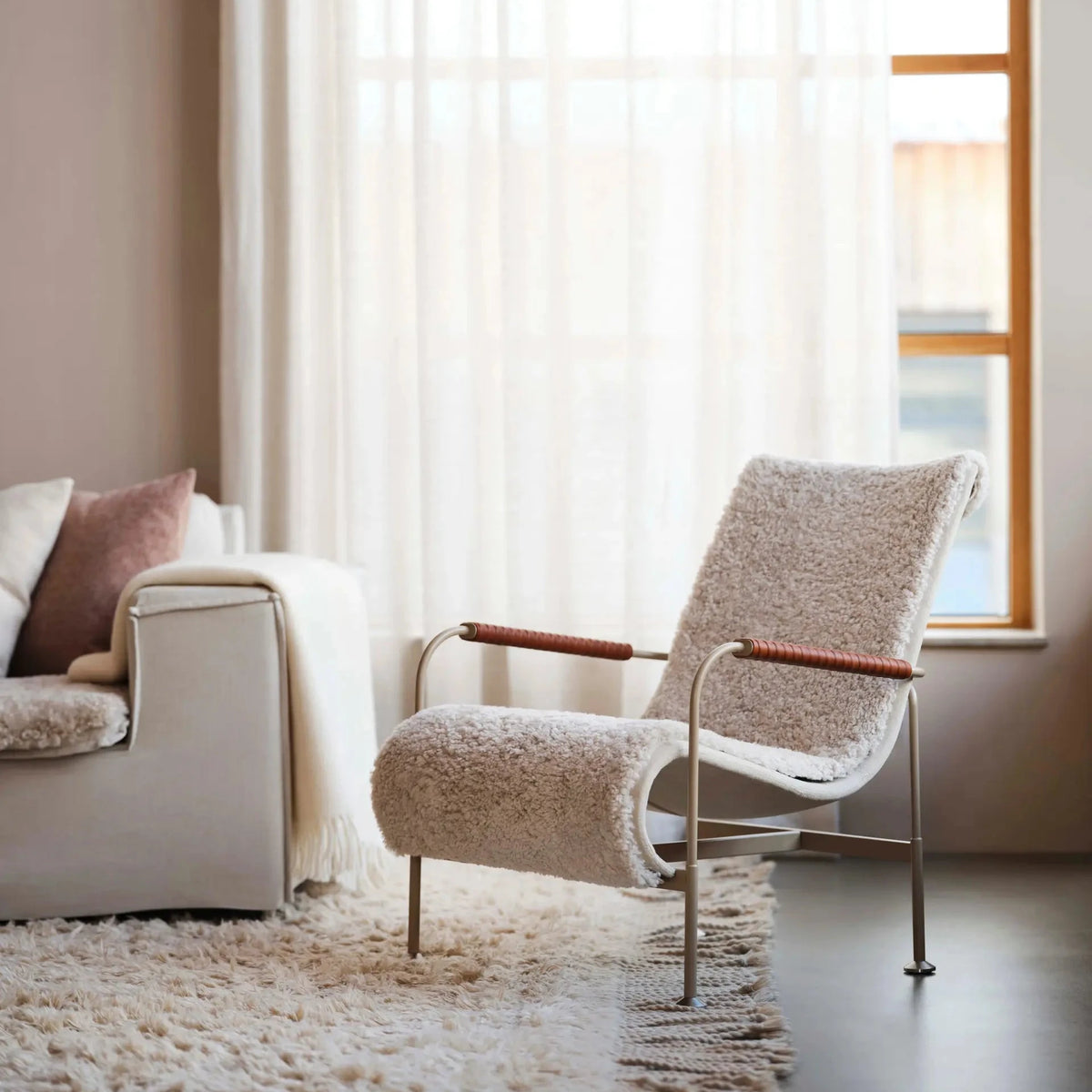 A mid-century modern lounge chair with a textured cream bouclé seat and back, featuring light wood armrests and a chrome metal frame, positioned in a bright, contemporary living room next to a sofa.