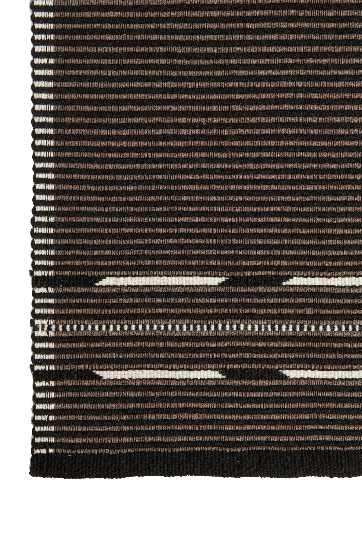 A close-up of a woven textile or rug showing horizontal stripes in black, dark brown, and off-white, with a ribbed black edge and fringe on the left side.