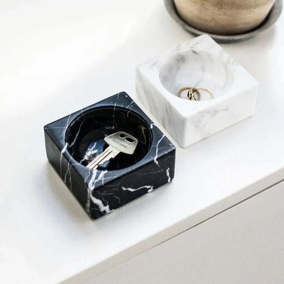 Square bowls in black and white marble holding keys and rings on a white surface